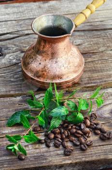 empty cezve on wooden background with scattered coffee beans and mint.