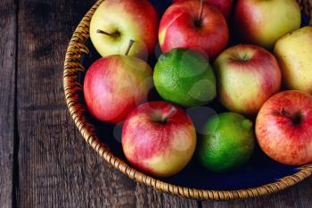 Harvest ripe apples and lime in stylish dish on wooden background
