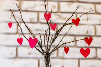 Bouquet of branches with red hearts on white brick wall background