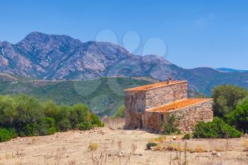 Rural landscape with small abandoned stone house and mountains on the horizon. Piana region, South Corsica, France