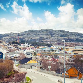 Rorvik, Norwegian town with colorful wooden houses on rocky hills under bright cloudy sky