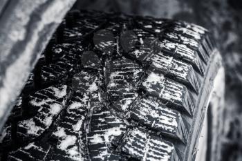 Snow tire with metal studs, which improve traction on icy surfaces, close-up photo of car wheel with selective focus