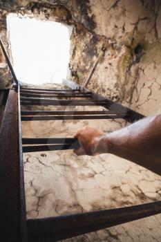 Rusty metal ladder with male hand holding it, empty mine interior with glowing end 