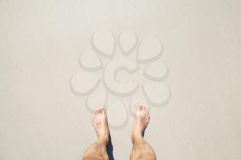 Male bare feet stand on white coastal sand, top view photo with copy space area