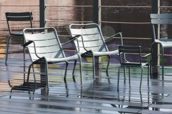 Empty outdoor gray metal chairs stand on wet pier