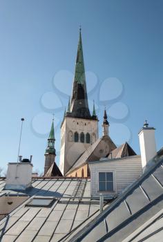 Houses with metal roofs and church St. Olaf above blue sky. Old Tallinn, Estonia