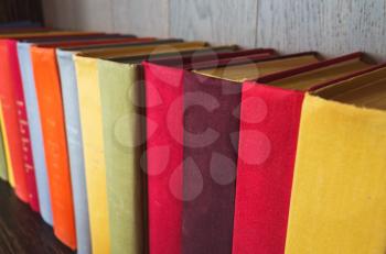 Colorful old books stand in a row on wooden shelf