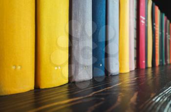 Books stand in a row on dark wooden shelf