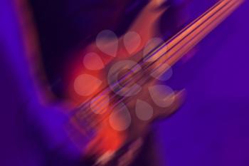 Blurred rock music background, bass guitar player on a stage with blue and purple colorful illumination