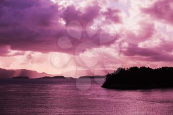 Norwegian coastal landscape with sun beams in dramatic sky. Purple tonal filter effect