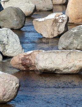 Stones with snow in shallow spring stream