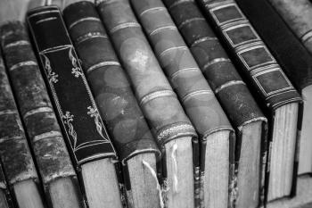 Old books with leather covers lay on the shelf, vintage stylized monochrome photo