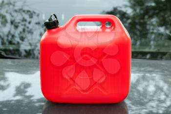 New red plastic jerrycan stands on a car hood