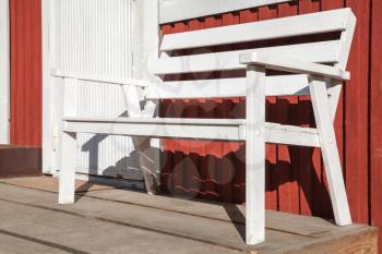 White wooden bench stands on terrace of Scandinavian red wooden house