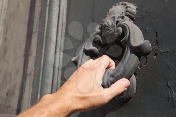 Male hand knocking old black door with metal ring knocker