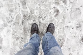 Male feet in blue jeans standing on wet dirty snow