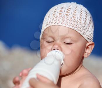 Little Caucasian baby drinks milk from the white plastic bottle