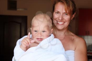 Young Caucasian mother holds with smile her baby in white cotton towel after the bath
