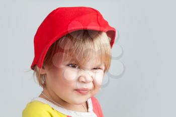 Studio portrait of funny smiling baby girl in red baseball cap over gray wall background