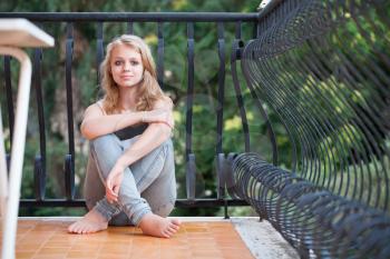 Beautiful blond Caucasian teenage girl sits on balcony, outdoor summer portrait