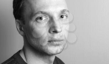 Young serious Caucasian man, close-up studio portrait over gray wall background, black and white photo