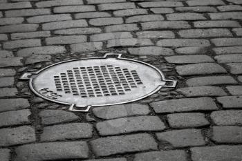 Old sewer manhole on dark cobblestone pavement