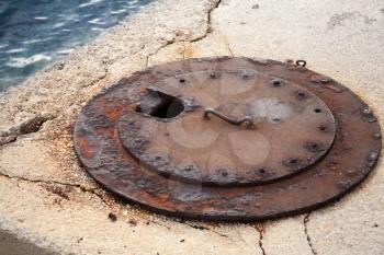 Old rusted sewer manhole with handle on concrete sea coast