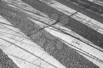 Tire tracks over pedestrian crossing road marking on dark asphalt
