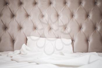 Luxury empty bedroom interior fragment, soft pink headboard, white bedding sheet and pillow lay on wide empty bed