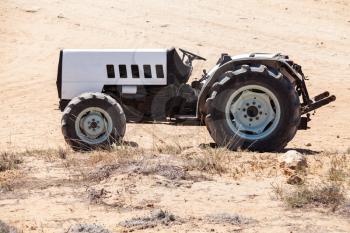 Empty gray tractor with black details stands on sandy ground in summer