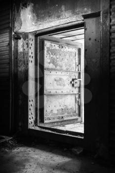 Abstract dark grungy industrial interior with rusted wall and open heavy steel door, black and white photo