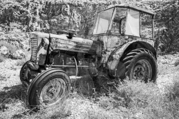 Old abandoned rusted tractor stands on dry grass, side view. Black and white photo