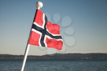 Norwegian national flag waving over blue sky background, vintage toned photo