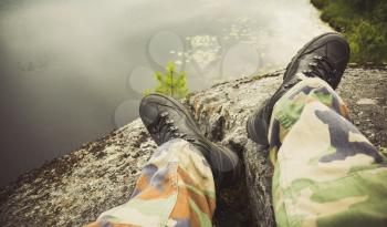 Male feet in camouflage pants and black rough shoes. Travel lifestyle background. Vintage tonal correction photo filter, old style effect