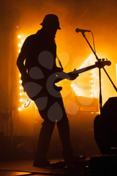 Silhouette of bass electric guitar player on the stage with microphone and bright warm illumination, live music theme