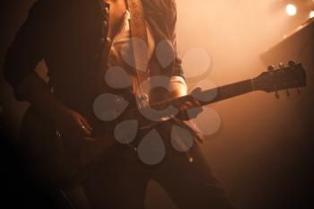 Rock and roll music background, electric guitar player on a stage with warm scenic illumination, soft selective focus