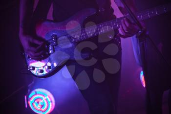 Live rock music background, electric bass guitar player in purple stage lights, closeup photo with soft selective focus