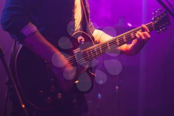 Electric guitar player on stage with purple scenic illumination, soft selective focus