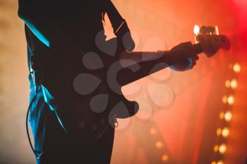 Silhouette of bass guitar player with colorful stage illumination, live rock music theme