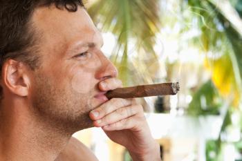 Young European man smokes big cigar, closeup profile portrait with selective focus. Dominican Republic