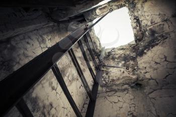 Old empty abandoned bunker interior with rusted metal ladder going up to glowing manhole