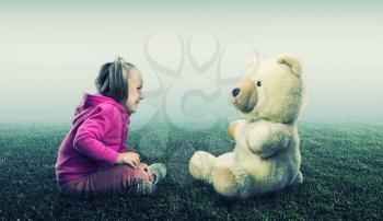 Small cute girl sits and looks at toy bear on white and green background