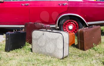 Many old suitcases standing on the grass near a red car