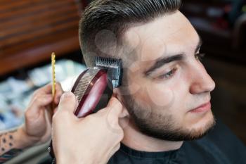 Side view of a young man having hair dress, barber working with hair clipper