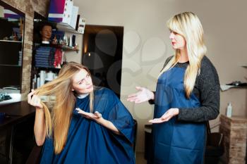 Beautiful girl showing her hair to hairdresser. Hairdressing salon.