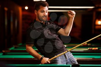 Player glad that has hammered a difficult sphere. Poolroom on the background.