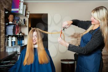 Young woman with long hair at hairdresser.Stylist making hairstyle with scissors and comb.