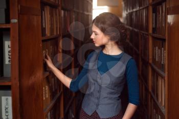 Young woman selecting book from library shelf. Knowledge, education and studying concept.