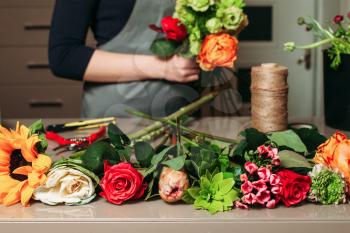 Florist with bouquet of roses at work. Woman in apron creating bouquet of flowers.
