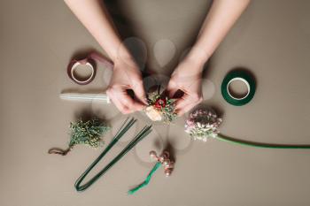 Top view of hands of young woman florist creating bouquet of flowers on grey background.